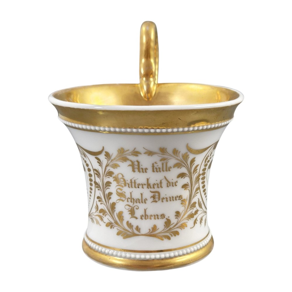 An antique white and gilt porcelain presentation cup with an elevated loop handle sitting on a matching gilded saucer. View IX