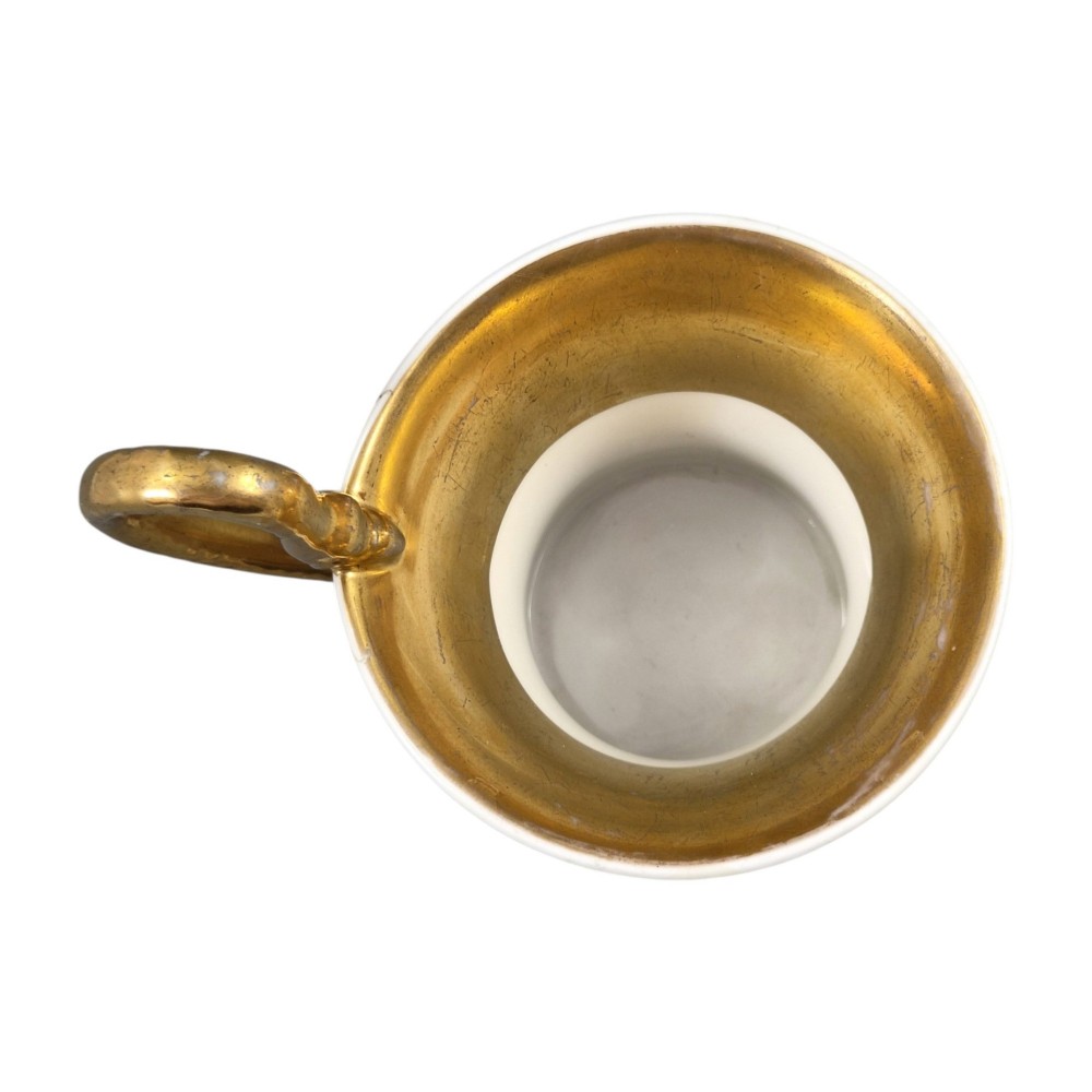 An antique white and gilt porcelain presentation cup with an elevated loop handle sitting on a matching gilded saucer. View XI