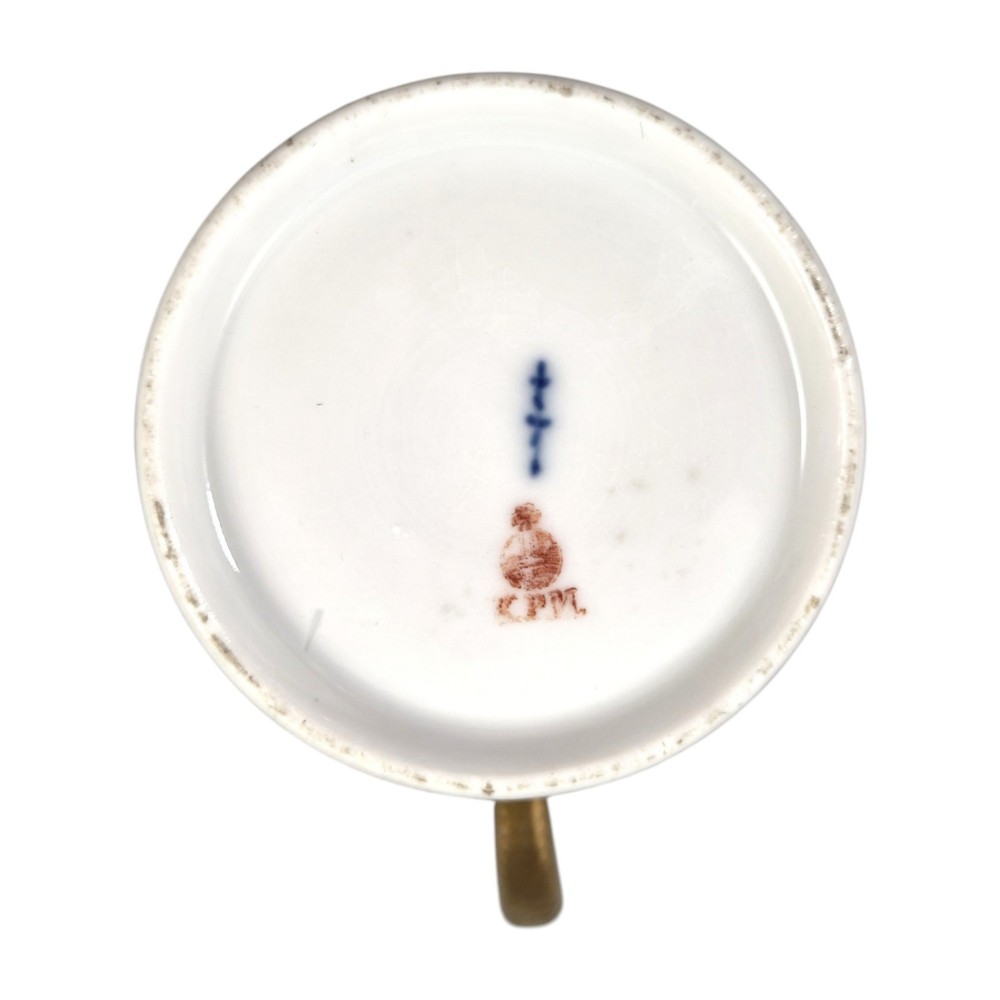 An antique white and gilt porcelain presentation cup with an elevated loop handle sitting on a matching gilded saucer. View XII