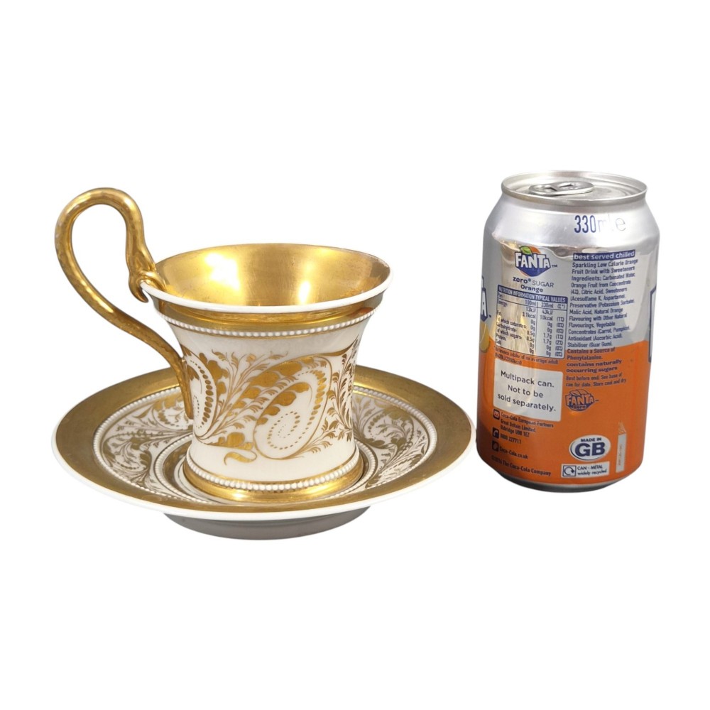 An antique white and gilt porcelain presentation cup with an elevated loop handle sitting on a matching gilded saucer. View XIII