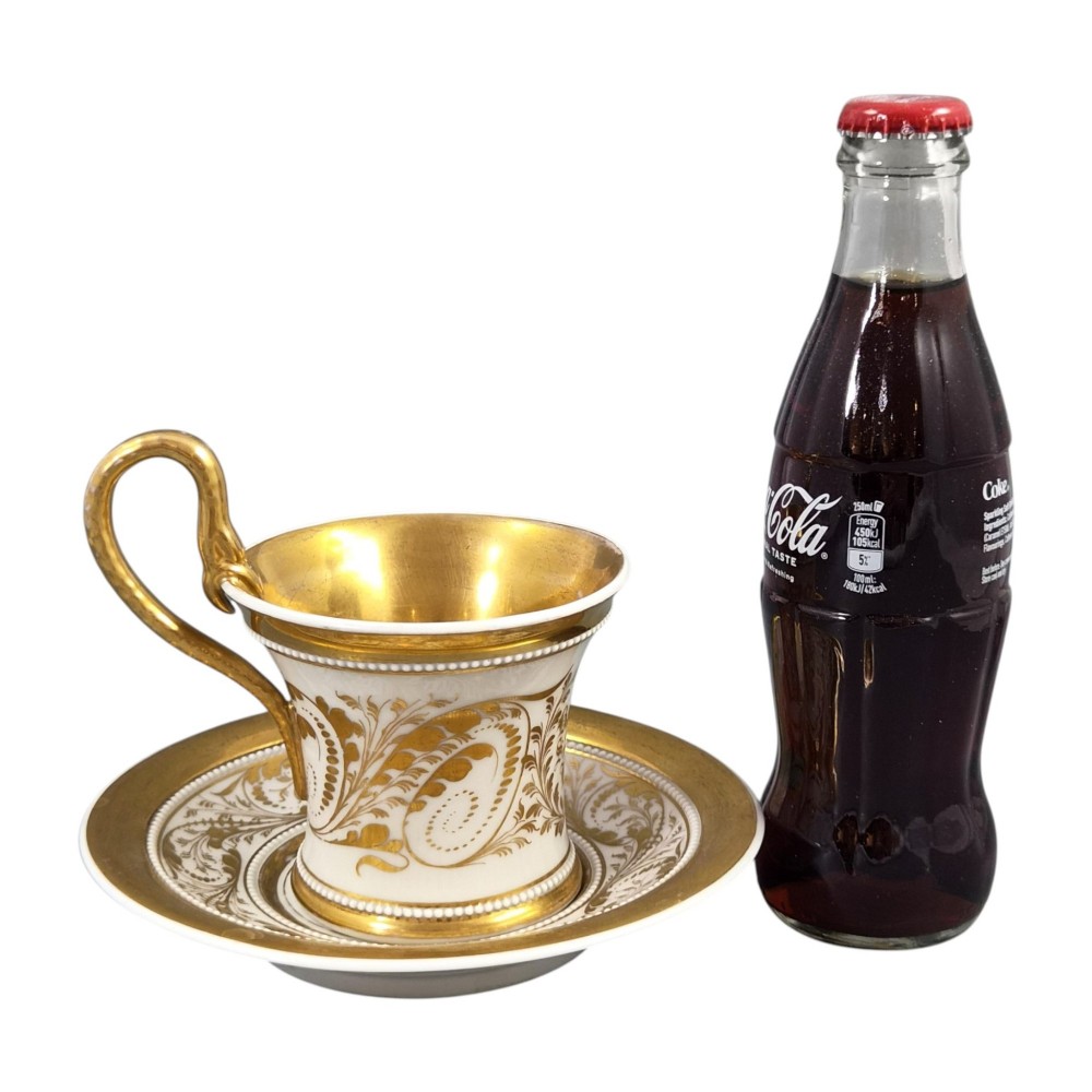 An antique white and gilt porcelain presentation cup with an elevated loop handle sitting on a matching gilded saucer. View XIV