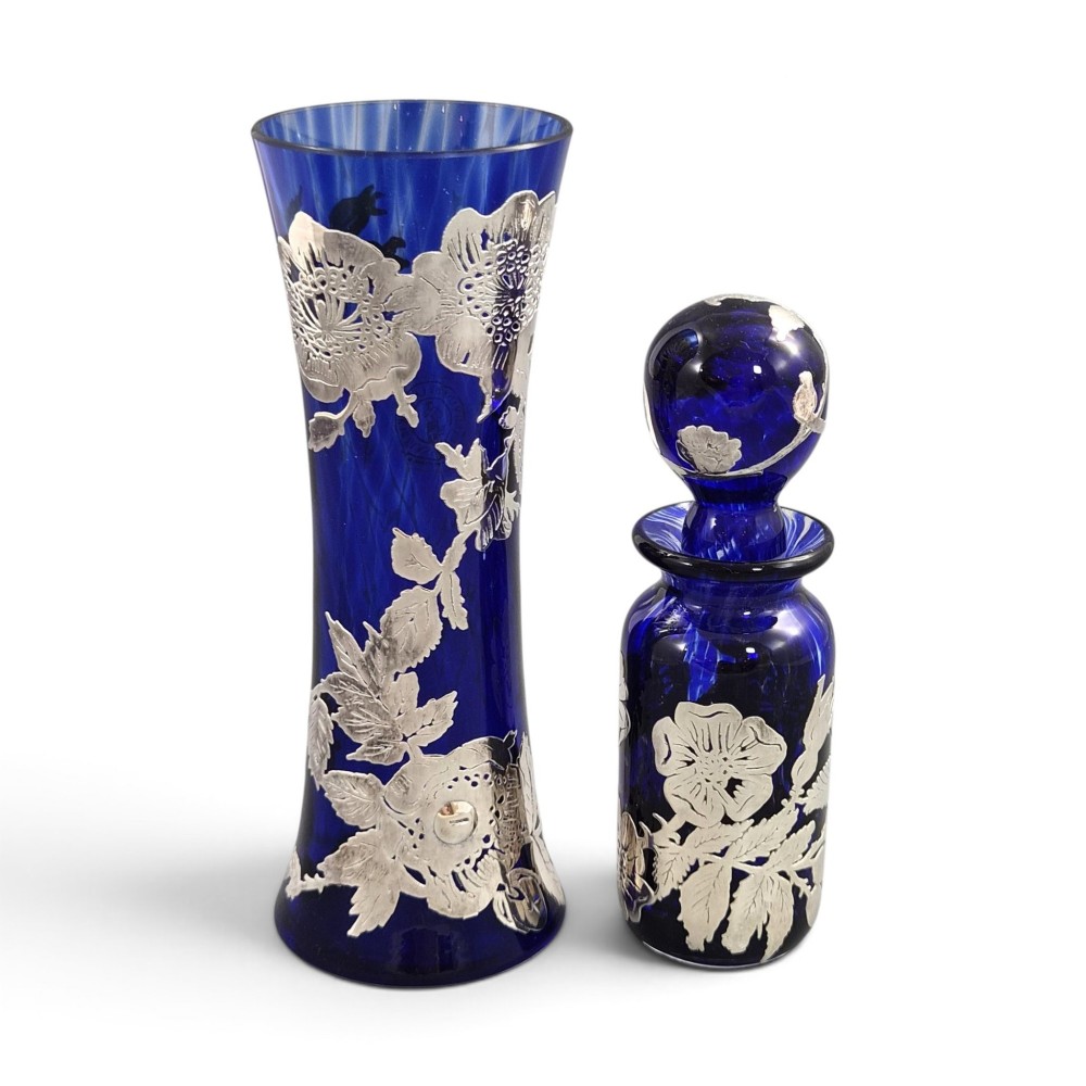 A cobalt blue glass vase and matching perfume bottle with stopper, both featuring intricate sterling silver floral overlay.