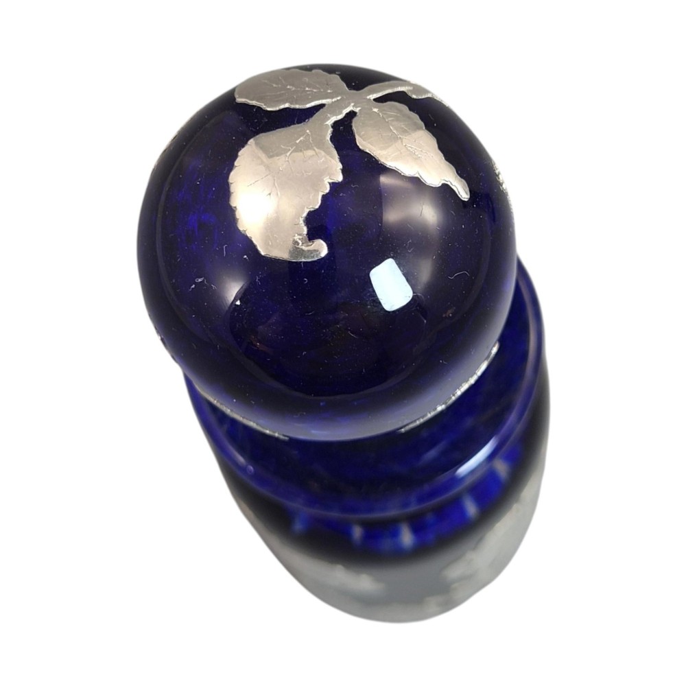 A cobalt blue glass vase and matching perfume bottle with stopper, both featuring intricate sterling silver floral overlay. View X