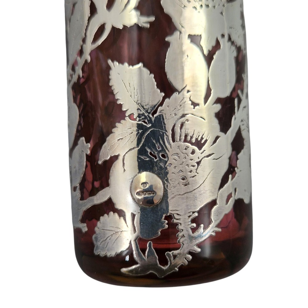 A three-piece ruby red glass vanity set featuring floral sterling silver overlay details across two stoppered bottles and a cylindrical beaker. View IX