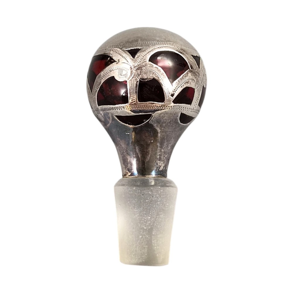 A three-piece ruby red glass vanity set featuring floral sterling silver overlay details across two stoppered bottles and a cylindrical beaker. View XV