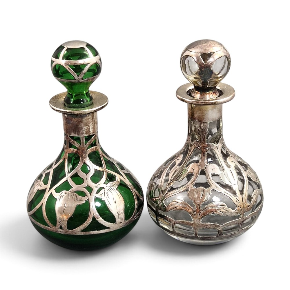 A pair of Art Nouveau perfume bottles featuring detailed sterling silver overlay in intricate floral lattice patterns on green and clear glass bases with matching glass stoppers.