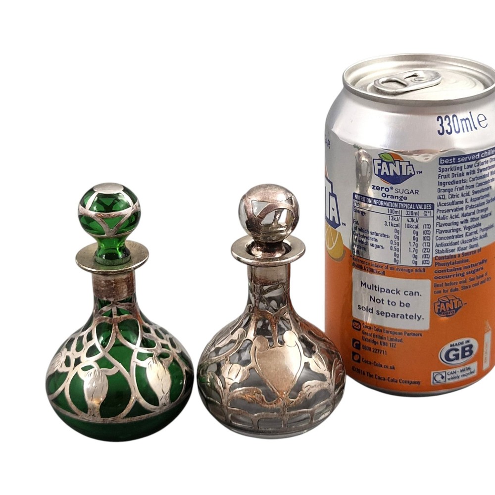 A pair of Art Nouveau perfume bottles featuring detailed sterling silver overlay in intricate floral lattice patterns on green and clear glass bases with matching glass stoppers. View V