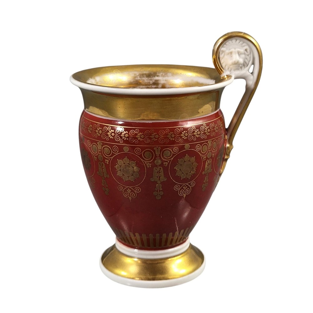 A red and gilded French Empire porcelain cabinet cup and matching saucer featuring a raised white lion mask handle detail. View VI