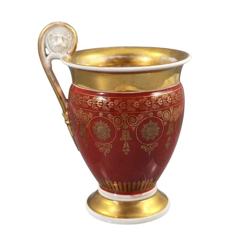 A red and gilded French Empire porcelain cabinet cup and matching saucer featuring a raised white lion mask handle detail. View VIII
