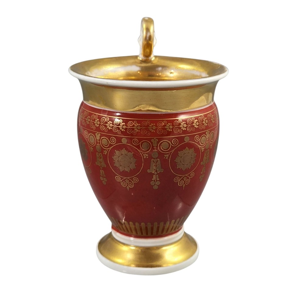 A red and gilded French Empire porcelain cabinet cup and matching saucer featuring a raised white lion mask handle detail. View IX