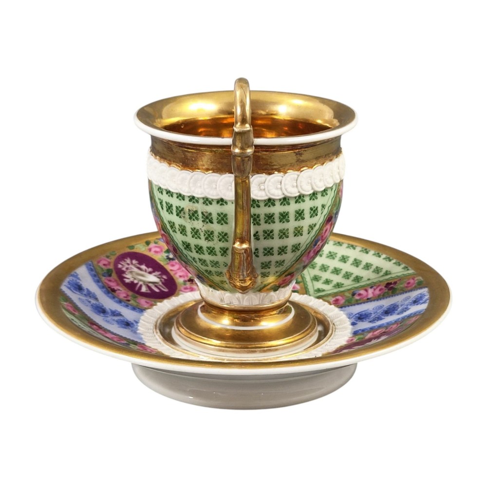 A nineteenth-century French Vieux Paris porcelain cabinet cup and matching saucer featuring gold gilding, multi-coloured hand-painted panels, and a high-loop lion mask handle. View II