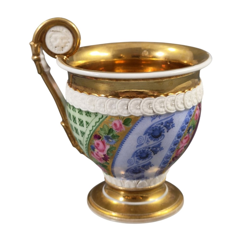 A nineteenth-century French Vieux Paris porcelain cabinet cup and matching saucer featuring gold gilding, multi-coloured hand-painted panels, and a high-loop lion mask handle. View X
