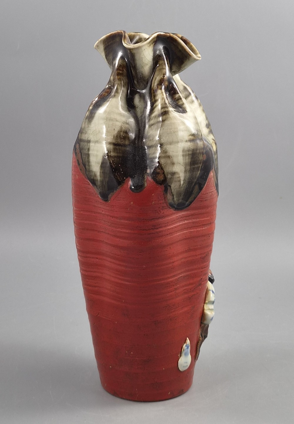 A tall Japanese Sumida Gawa ceramic vase featuring a ribbed red body, applied figures of climbing men, and a heavy flambe glaze around a pinched rim. View IV