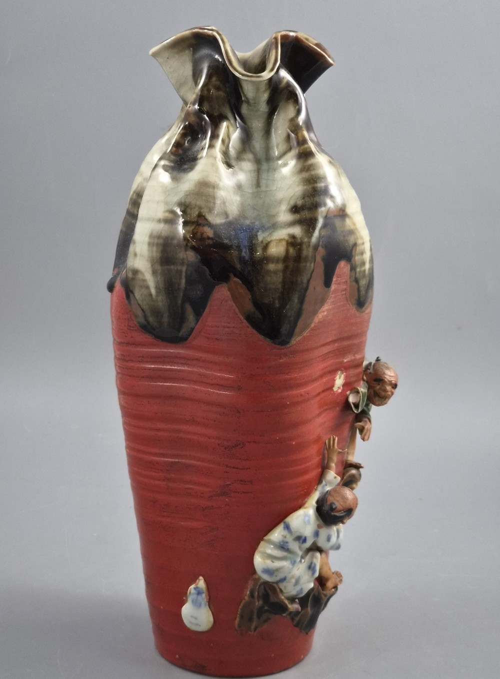 A tall Japanese Sumida Gawa ceramic vase featuring a ribbed red body, applied figures of climbing men, and a heavy flambe glaze around a pinched rim. View V