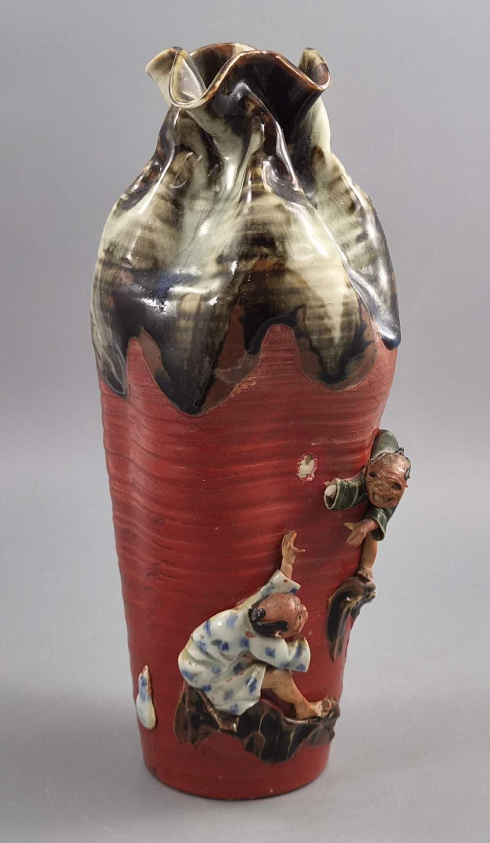A tall Japanese Sumida Gawa ceramic vase featuring a ribbed red body, applied figures of climbing men, and a heavy flambe glaze around a pinched rim. View VI