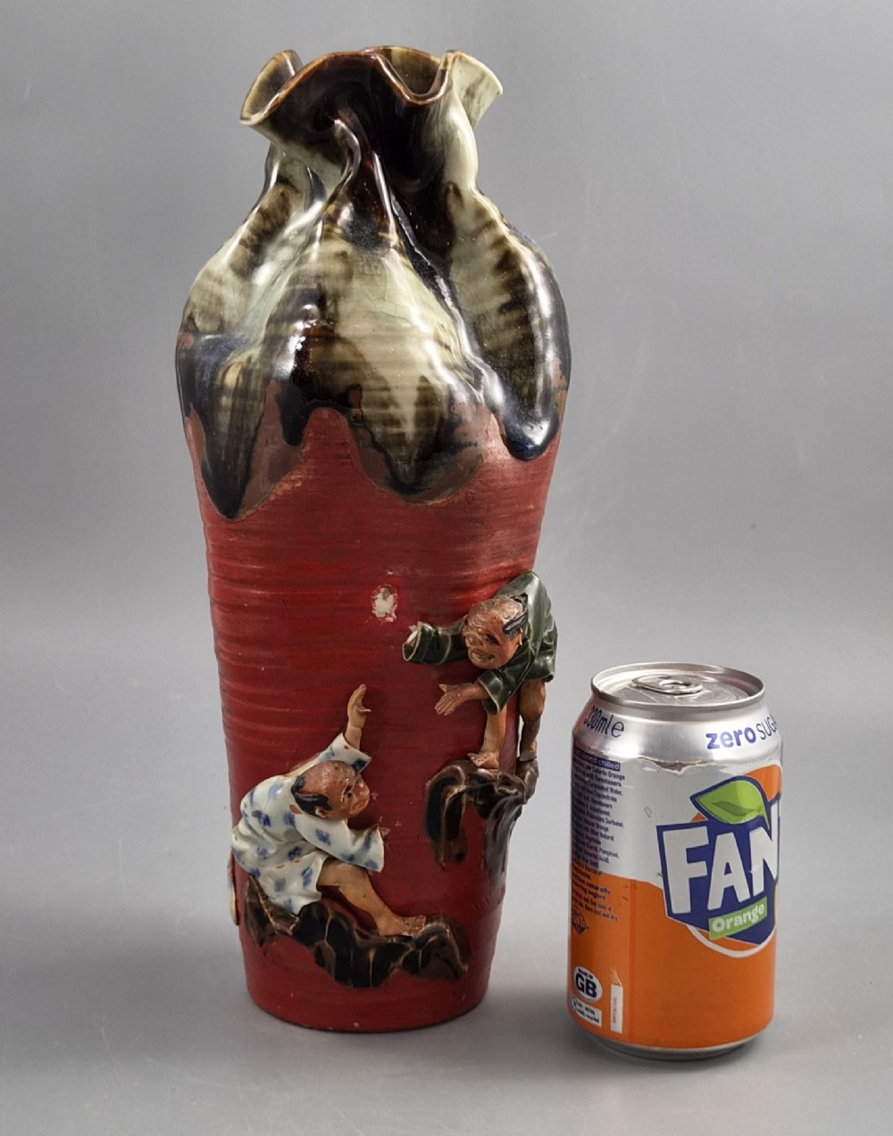 A tall Japanese Sumida Gawa ceramic vase featuring a ribbed red body, applied figures of climbing men, and a heavy flambe glaze around a pinched rim. View VIII