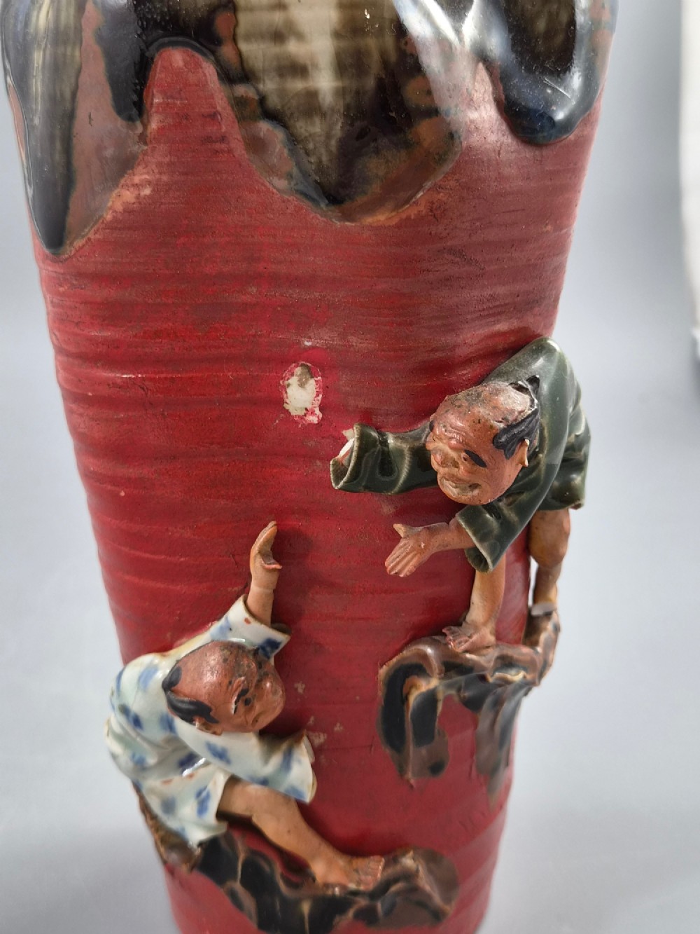 A tall Japanese Sumida Gawa ceramic vase featuring a ribbed red body, applied figures of climbing men, and a heavy flambe glaze around a pinched rim. View XI