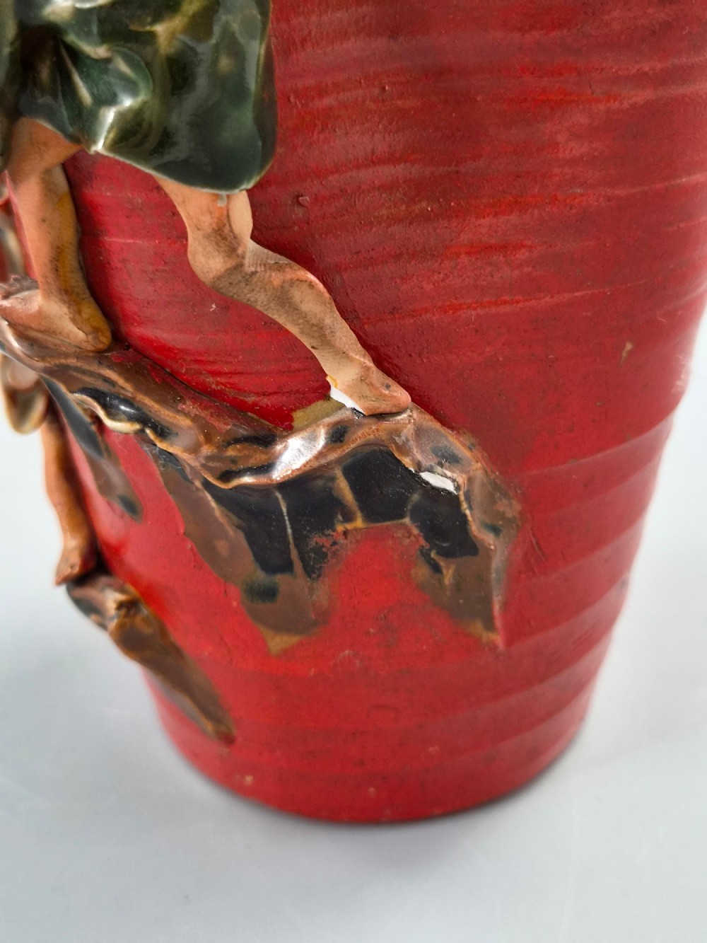A tall Japanese Sumida Gawa ceramic vase featuring a ribbed red body, applied figures of climbing men, and a heavy flambe glaze around a pinched rim. View XII