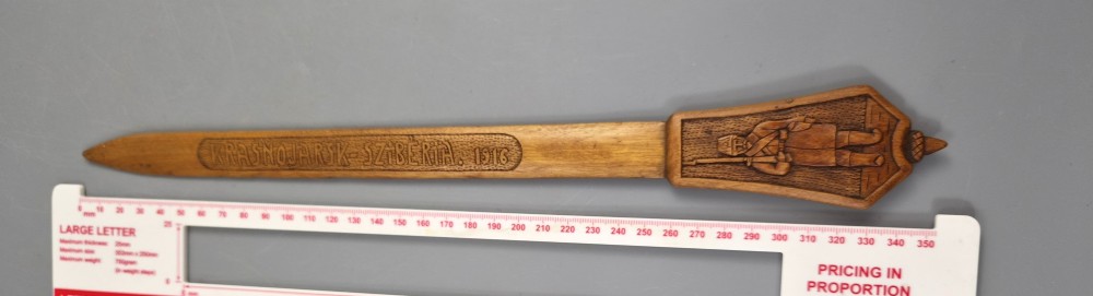 A hand-carved wooden letter opener featuring a relief carving of a soldier on the handle and carved text reading Krasnojarsk Sziberia 1916 on the blade. View X