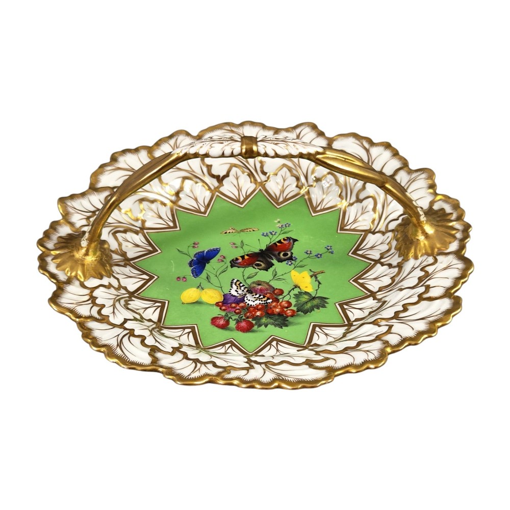 A Regency Flight, Barr and Barr Worcester porcelain handle basket featuring a bright green central reserve decorated with hand-painted butterflies and berries, surrounded by a leaf-moulded rim and gilt handle.