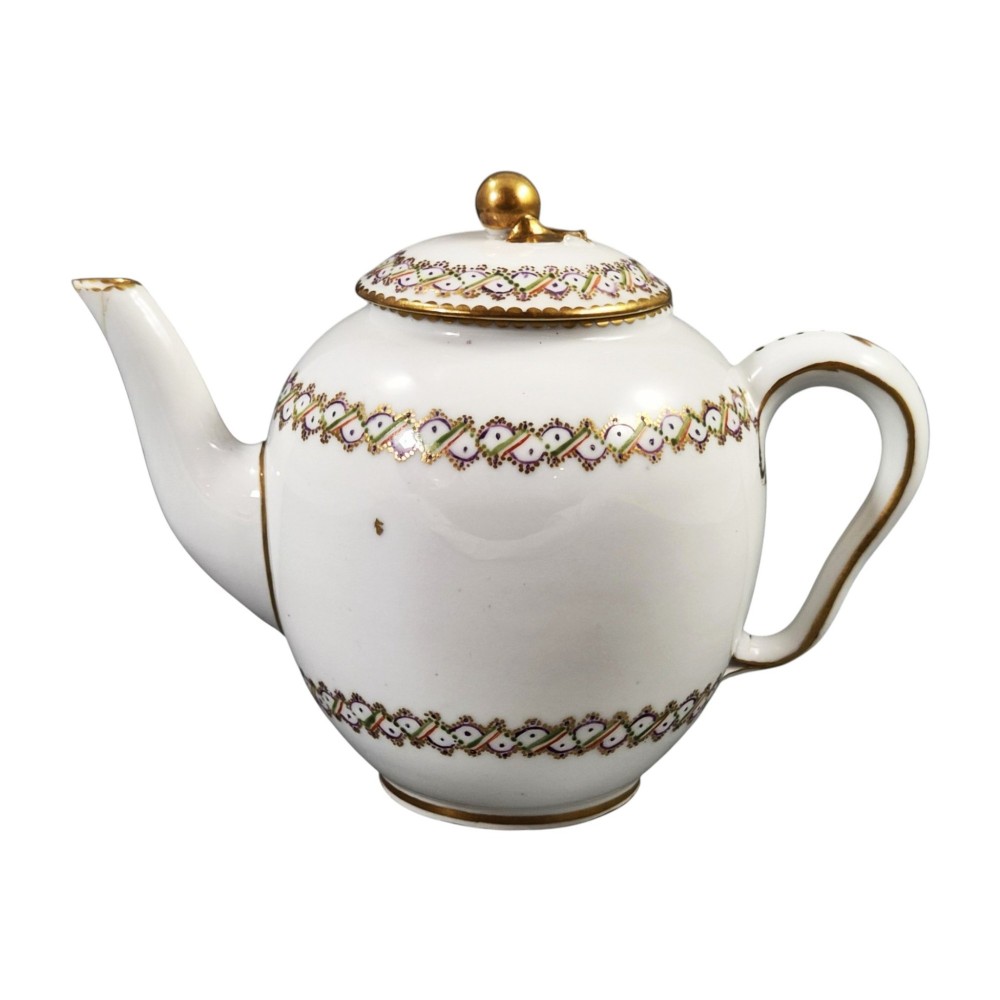 A white Sevres porcelain teapot featuring polychrome geometric enamel borders, gilt trim, a rounded body, and a gilded spherical lid finial. View V