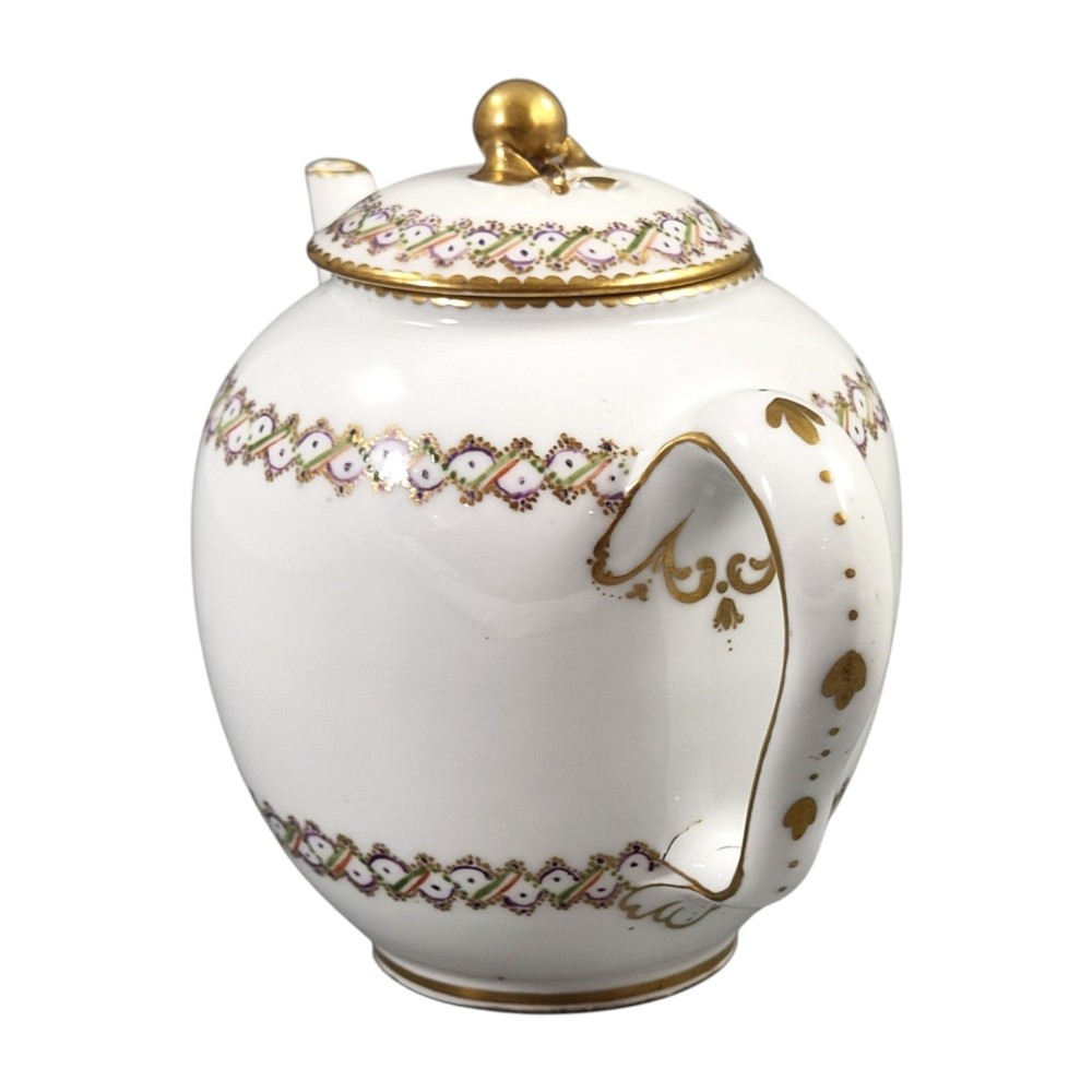 A white Sevres porcelain teapot featuring polychrome geometric enamel borders, gilt trim, a rounded body, and a gilded spherical lid finial. View VI