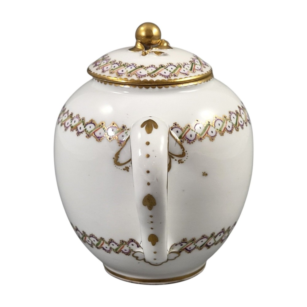 A white Sevres porcelain teapot featuring polychrome geometric enamel borders, gilt trim, a rounded body, and a gilded spherical lid finial. View VII