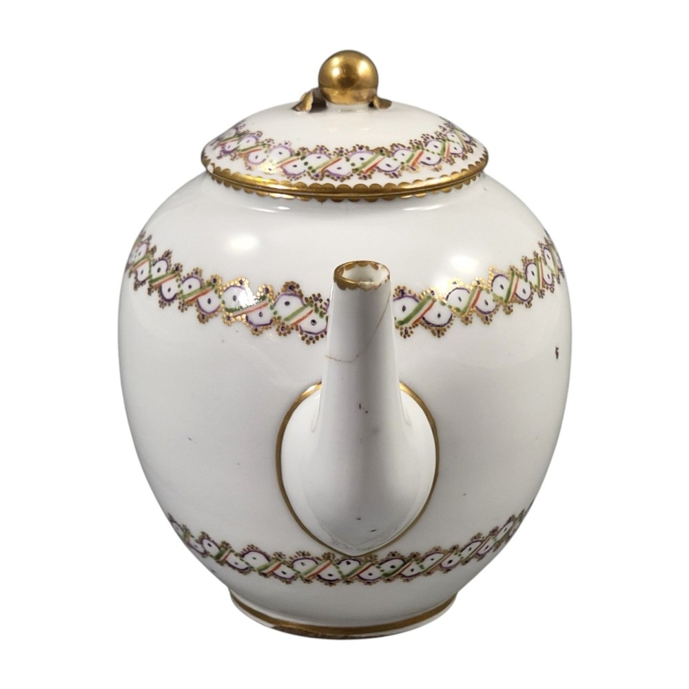 A white Sevres porcelain teapot featuring polychrome geometric enamel borders, gilt trim, a rounded body, and a gilded spherical lid finial. View VIII