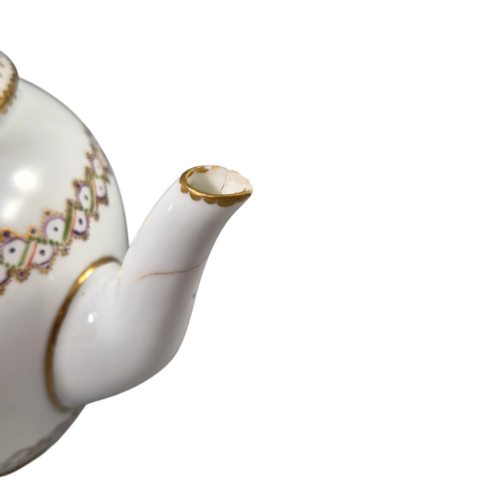 A white Sevres porcelain teapot featuring polychrome geometric enamel borders, gilt trim, a rounded body, and a gilded spherical lid finial. View XI