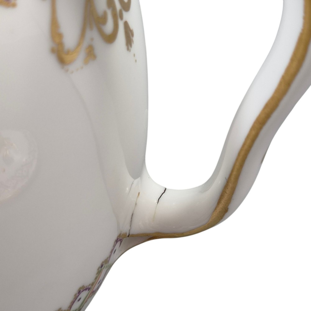A white Sevres porcelain teapot featuring polychrome geometric enamel borders, gilt trim, a rounded body, and a gilded spherical lid finial. View XII