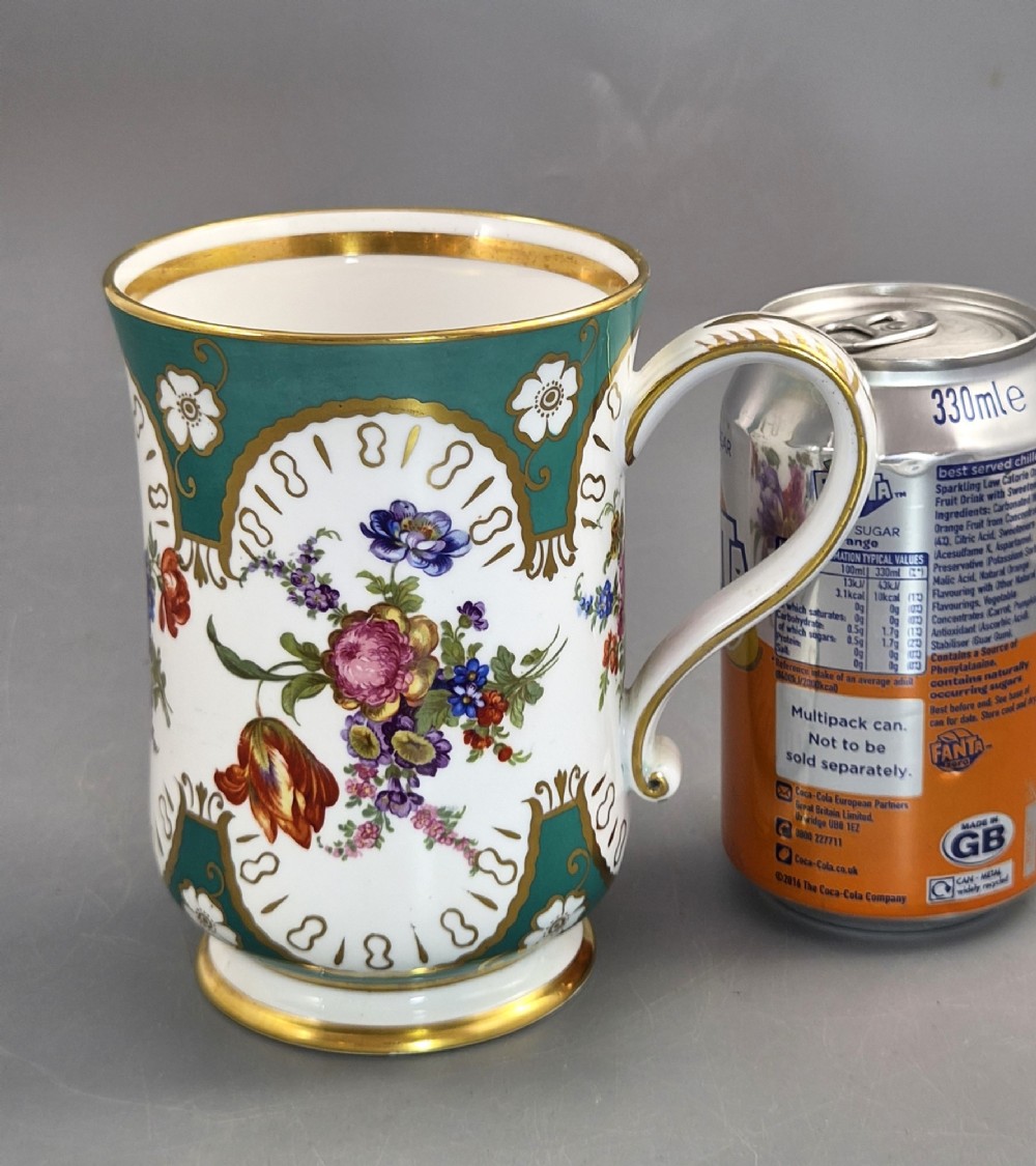 An antique French porcelain cabinet mug featuring a green ground border, hand-painted floral spray, ornate gilt accents, and a looped handle. View XI