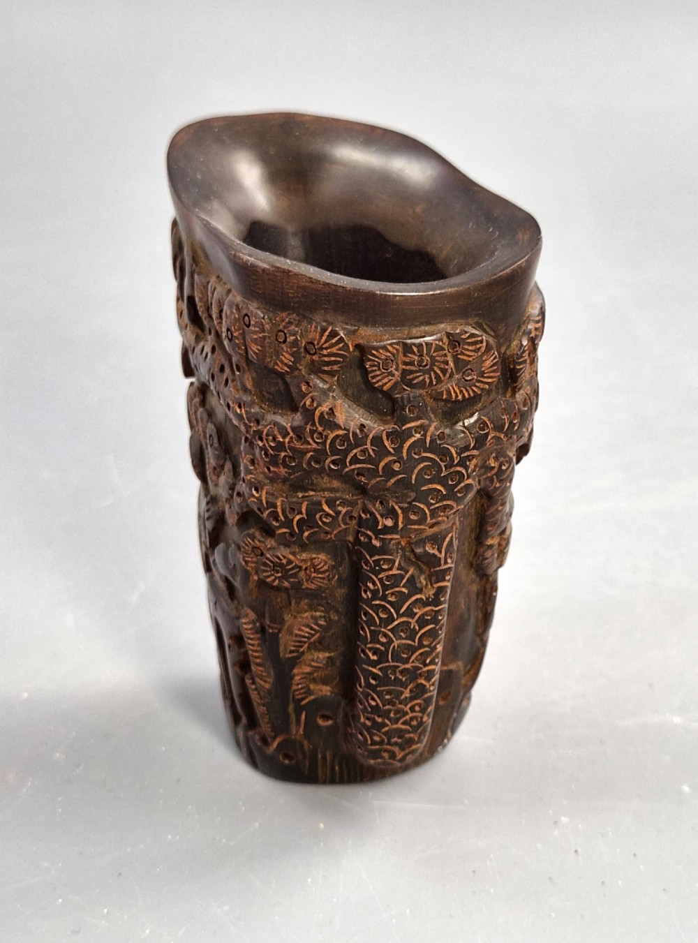 A dark brown carved water buffalo horn libation cup featuring relief carvings of immortals standing under pine trees. View II