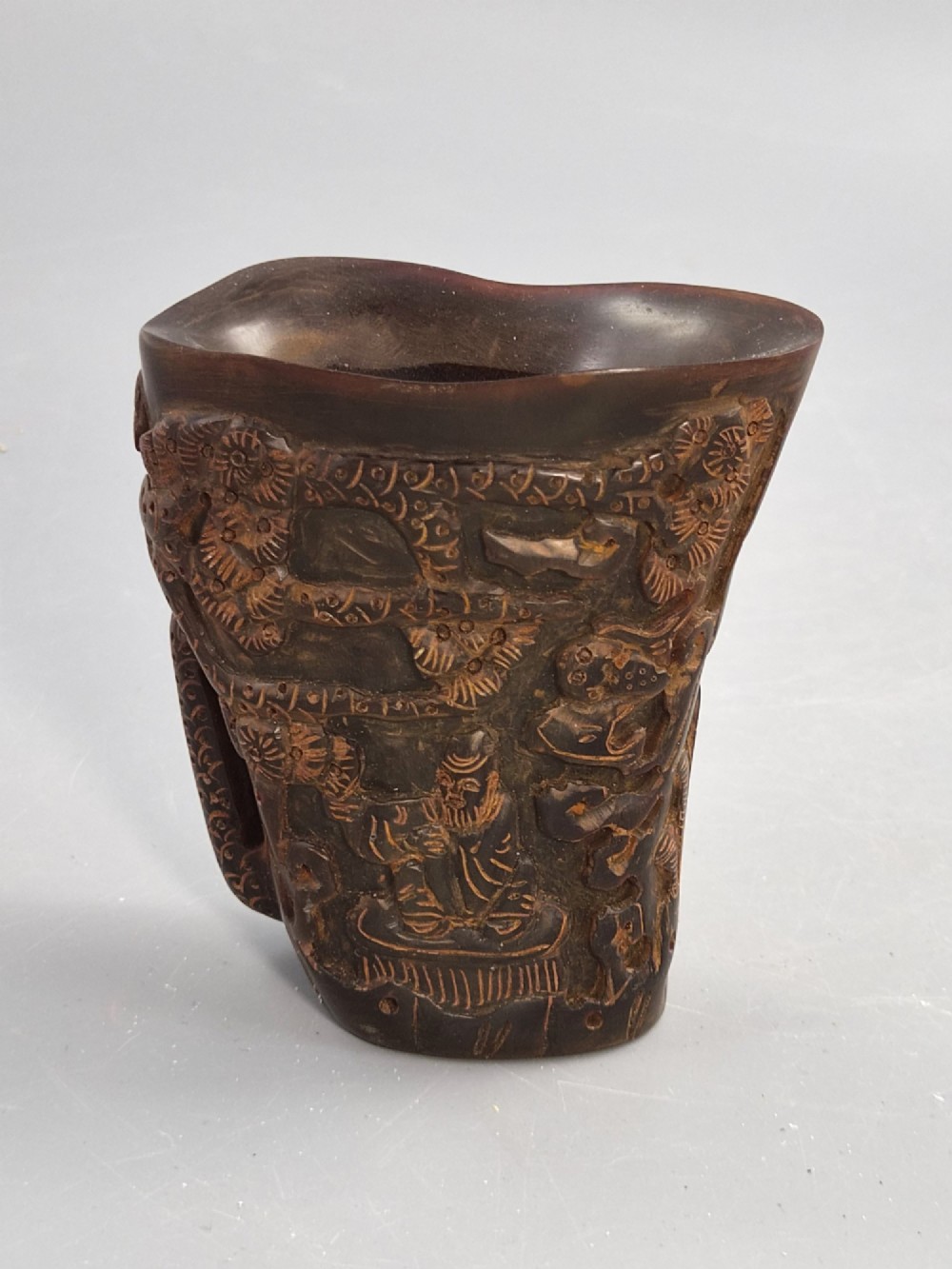 A dark brown carved water buffalo horn libation cup featuring relief carvings of immortals standing under pine trees. View IV