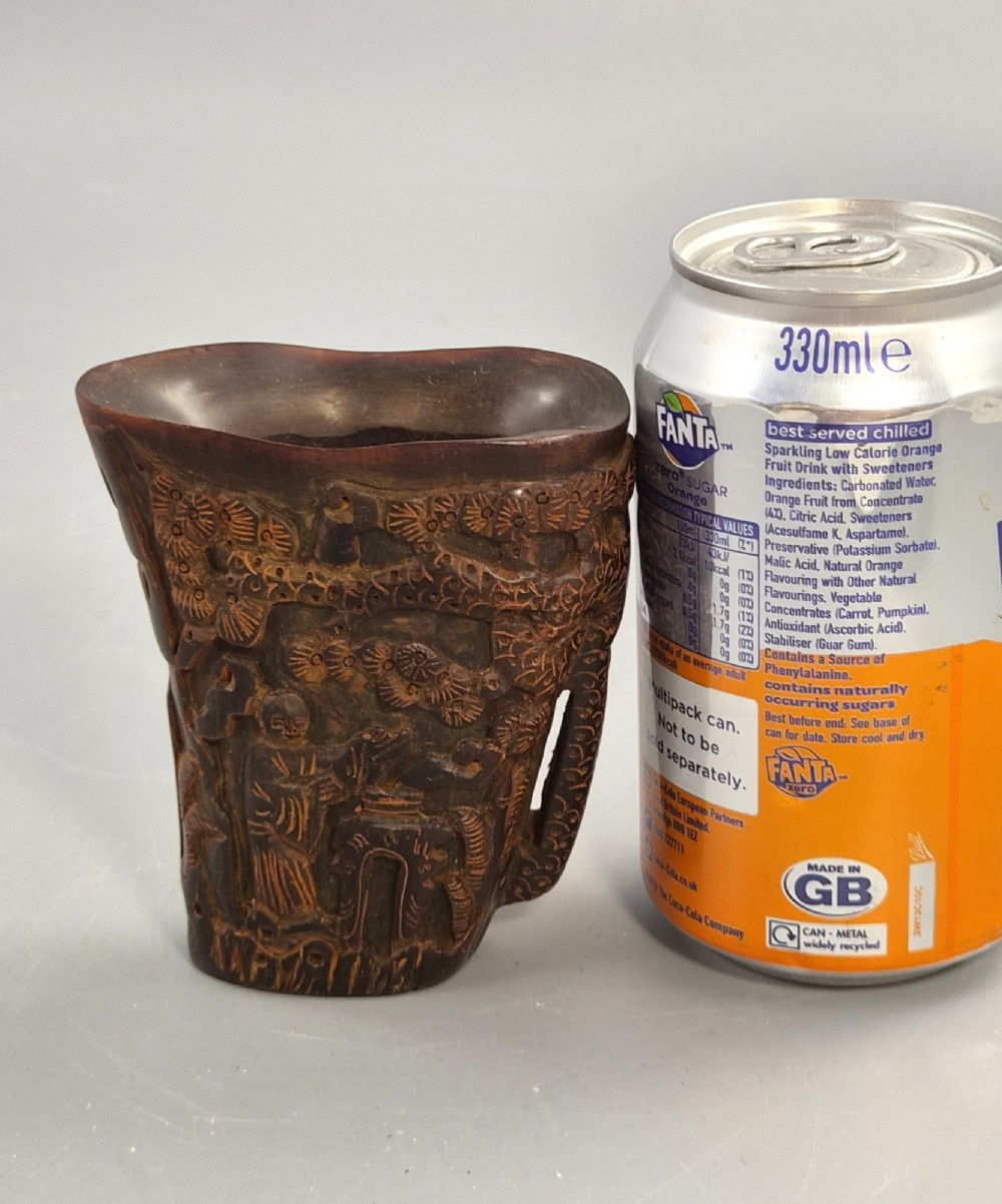 A dark brown carved water buffalo horn libation cup featuring relief carvings of immortals standing under pine trees. View IX