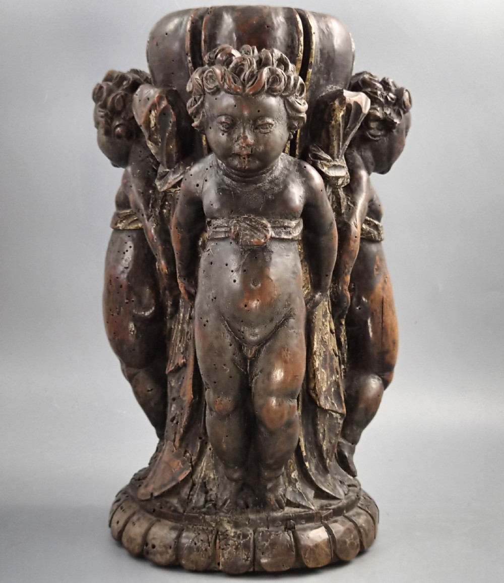 A dark carved walnut Italian Baroque torchiere base featuring three sculpted putti figures standing around a central fluted shaft on a gadrooned circular base.