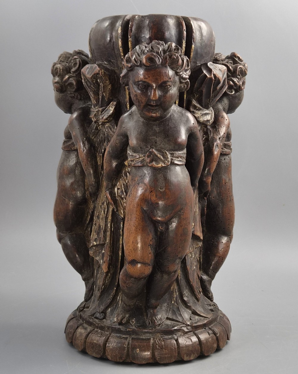 A dark carved walnut Italian Baroque torchiere base featuring three sculpted putti figures standing around a central fluted shaft on a gadrooned circular base. View III