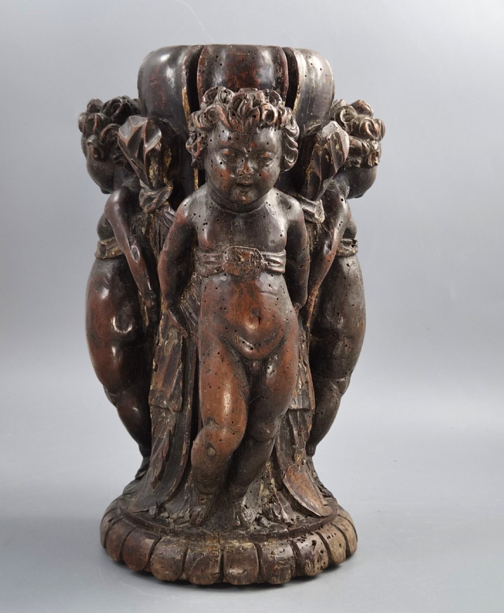A dark carved walnut Italian Baroque torchiere base featuring three sculpted putti figures standing around a central fluted shaft on a gadrooned circular base. View V