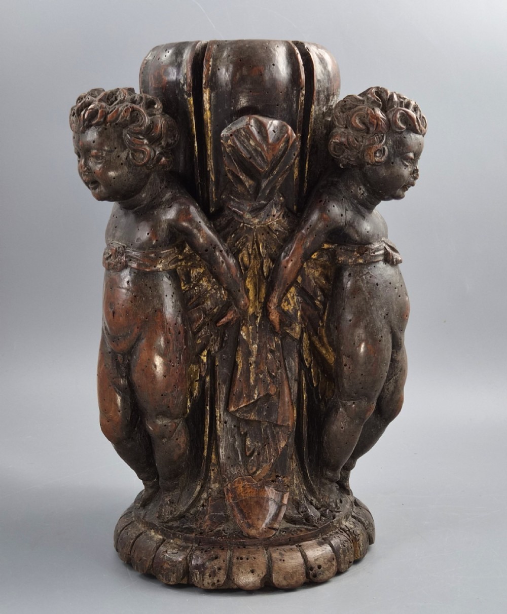 A dark carved walnut Italian Baroque torchiere base featuring three sculpted putti figures standing around a central fluted shaft on a gadrooned circular base. View VI