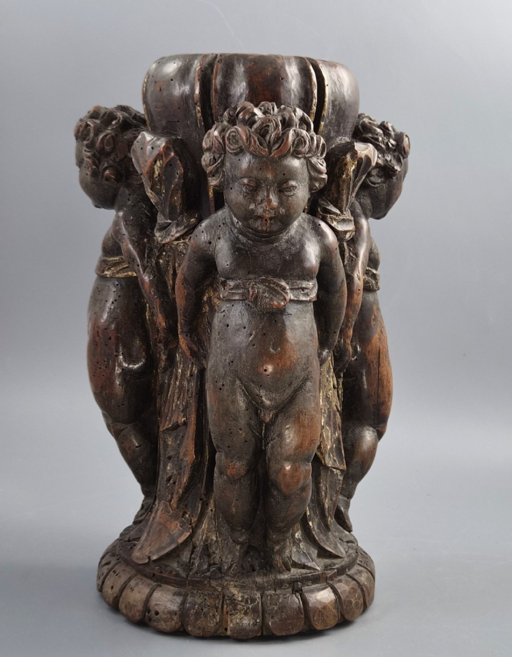 A dark carved walnut Italian Baroque torchiere base featuring three sculpted putti figures standing around a central fluted shaft on a gadrooned circular base. View VII