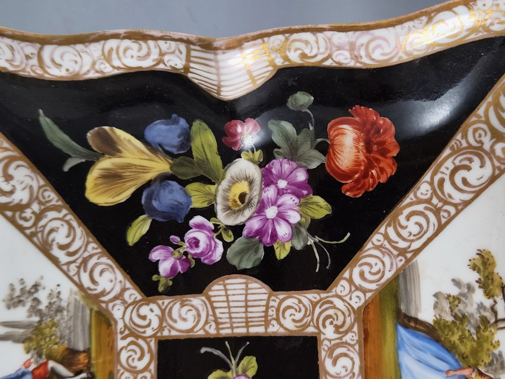 A square shaped Meissen porcelain dish decorated with hand-painted Watteau scenes, floral reserves on a black ground, and gilded scroll borders. View III