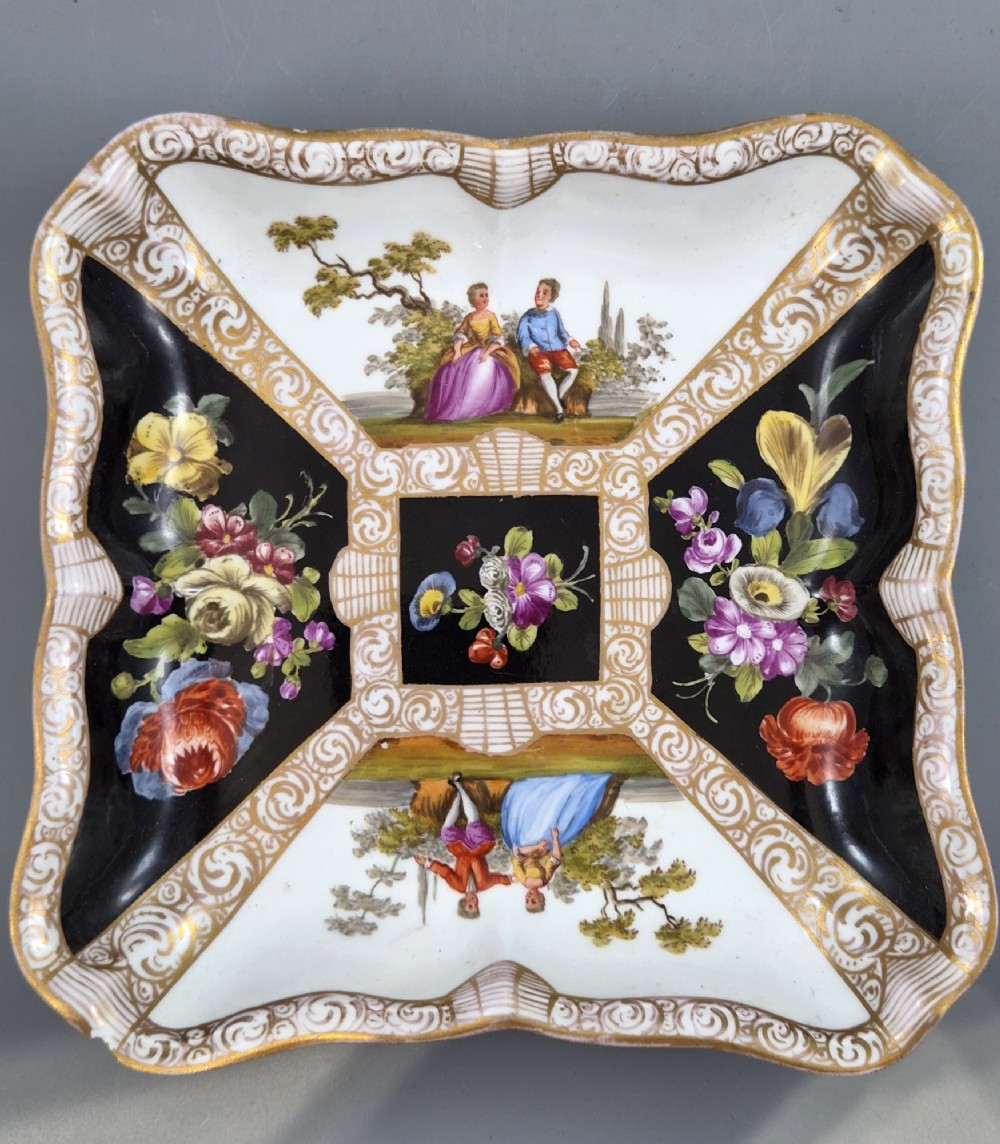 A square shaped Meissen porcelain dish decorated with hand-painted Watteau scenes, floral reserves on a black ground, and gilded scroll borders. View IV