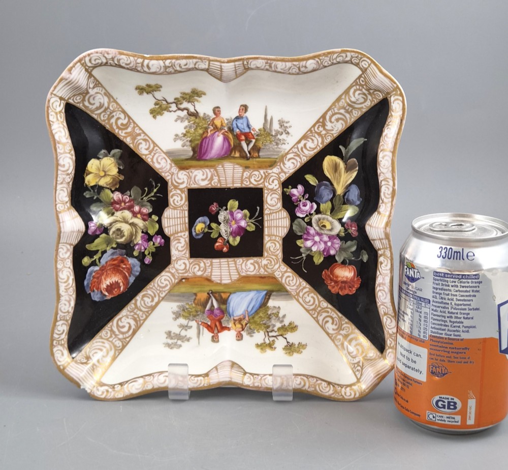 A square shaped Meissen porcelain dish decorated with hand-painted Watteau scenes, floral reserves on a black ground, and gilded scroll borders. View VI