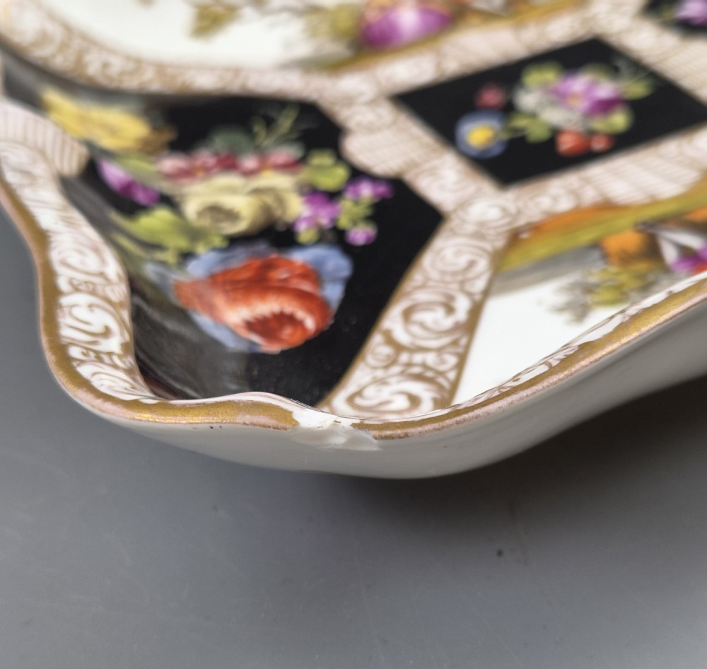 A square shaped Meissen porcelain dish decorated with hand-painted Watteau scenes, floral reserves on a black ground, and gilded scroll borders. View XII