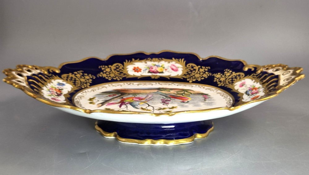 An oval porcelain dish featuring a dark cobalt blue rim with gold scrollwork, reticulated handles, floral panels, and a central hand-painted scene of colorful birds perched on branches. View VII