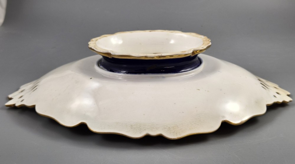 An oval porcelain dish featuring a dark cobalt blue rim with gold scrollwork, reticulated handles, floral panels, and a central hand-painted scene of colorful birds perched on branches. View XII