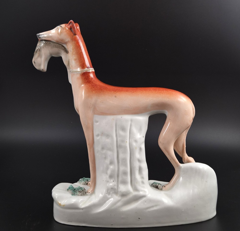 A pair of antique Victorian Staffordshire earthenware figures depicting standing orange greyhounds holding grey hares in their jaws on white bases. View VII