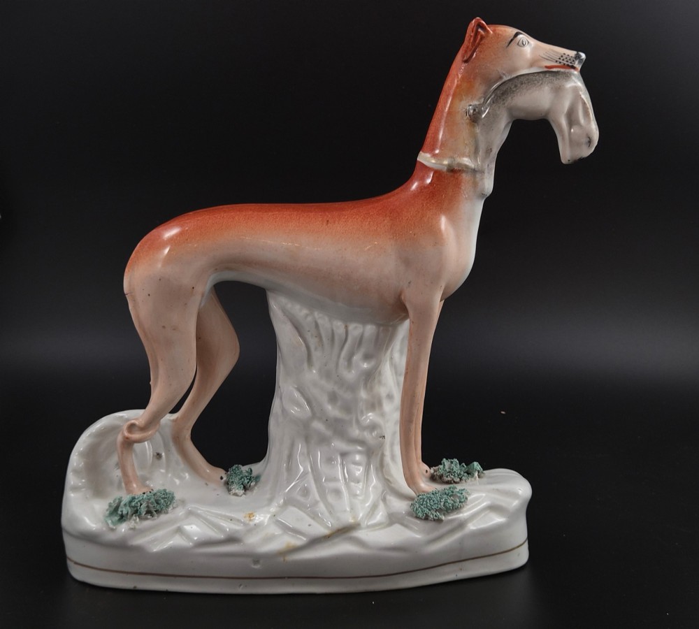 A pair of antique Victorian Staffordshire earthenware figures depicting standing orange greyhounds holding grey hares in their jaws on white bases. View X