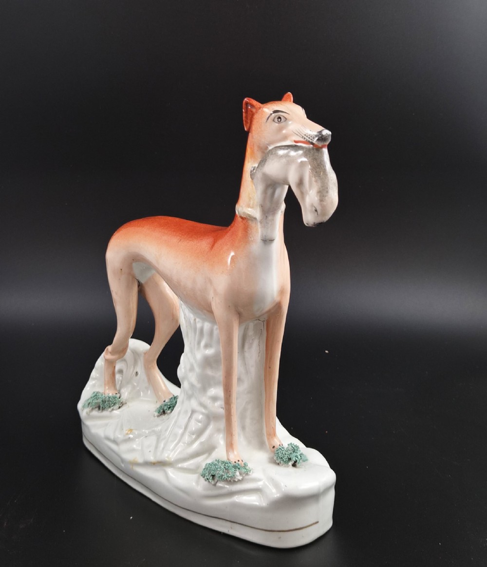 A pair of antique Victorian Staffordshire earthenware figures depicting standing orange greyhounds holding grey hares in their jaws on white bases. View XI