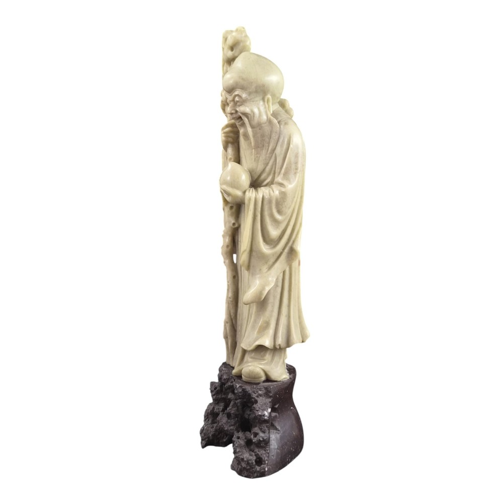 A late 19th-century carved pale soapstone figure of Shoulao holding a peach and staff, standing on a dark stone pierced rockwork base. View II