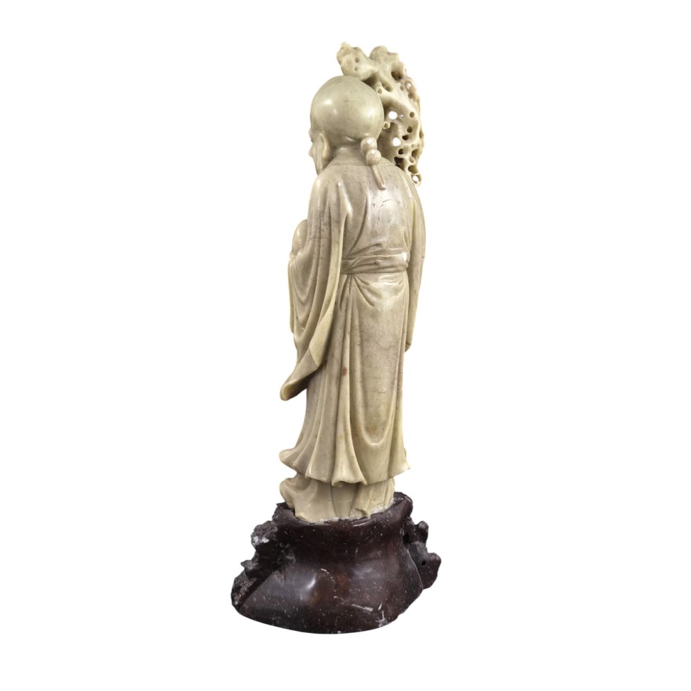 A late 19th-century carved pale soapstone figure of Shoulao holding a peach and staff, standing on a dark stone pierced rockwork base. View III
